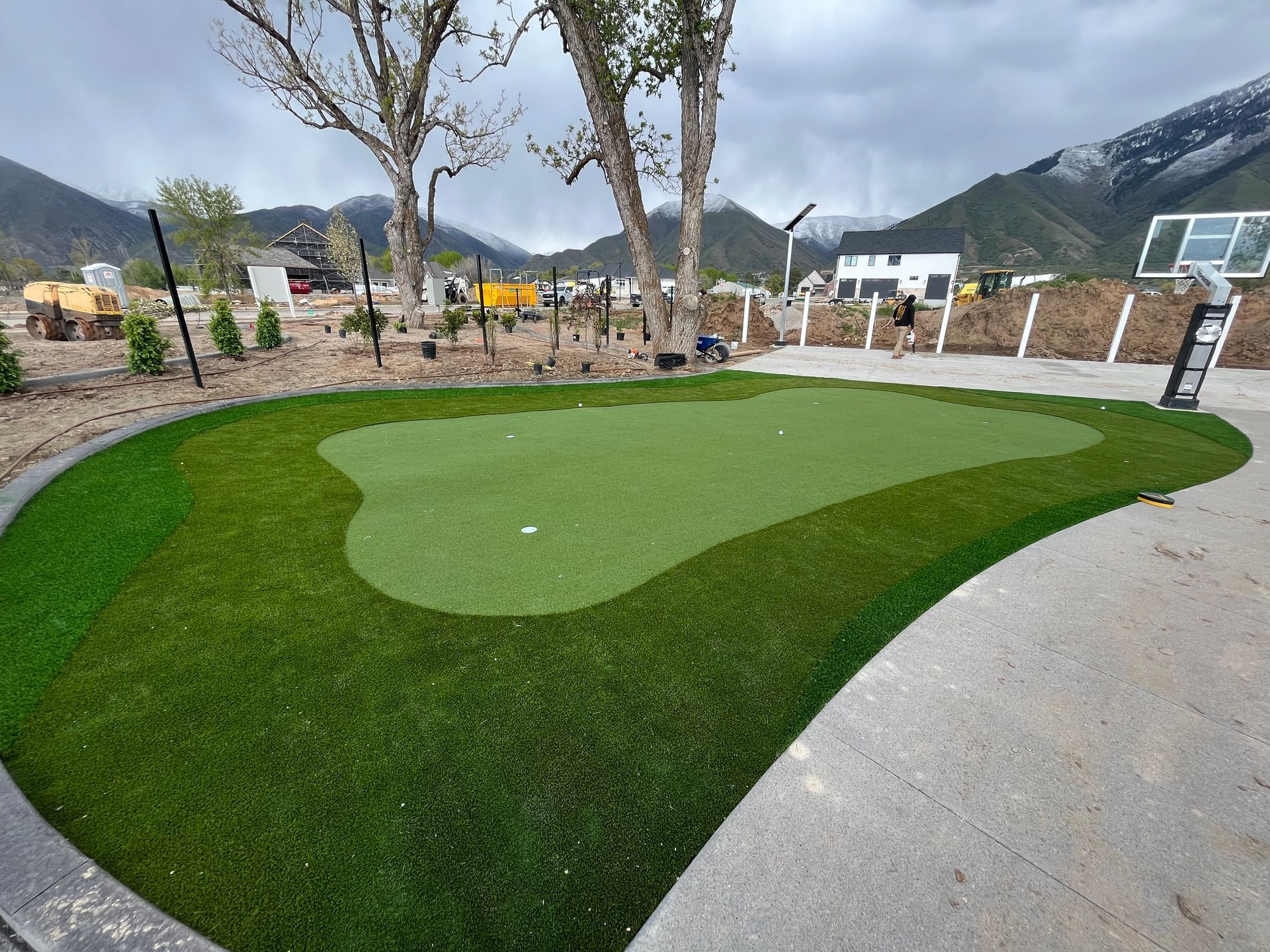 A golf putting green with a dark green inner circle and a lighter green surrounding it, with a mountain backdrop.