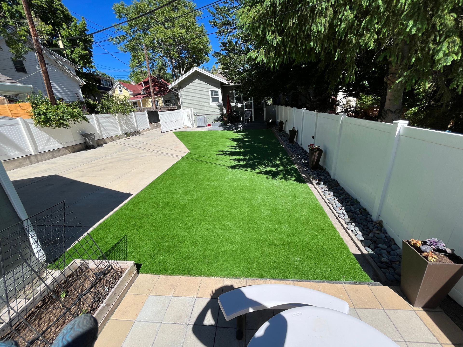 Backyard with artificial grass, patio, and white fence.