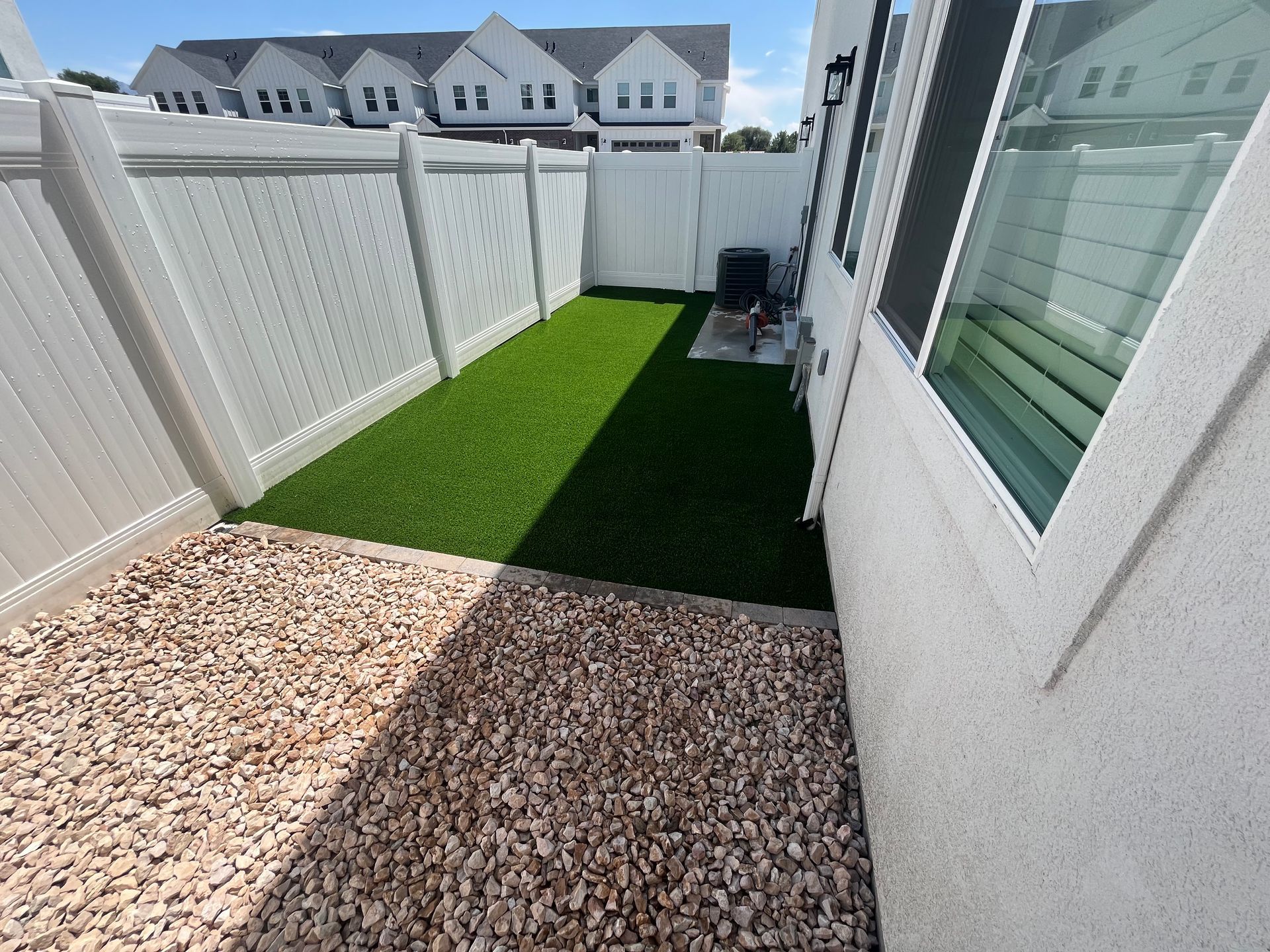 Small backyard with gravel and artificial turf, white fence.
