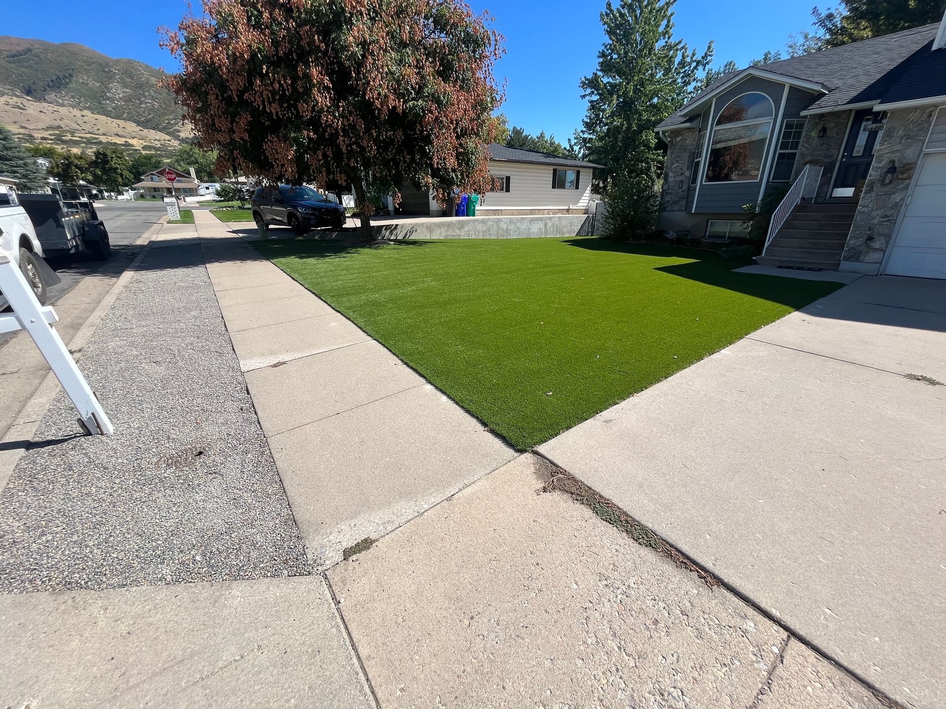 A house with a concrete driveway, gravel path, and a patch of green grass; mountains in the background.