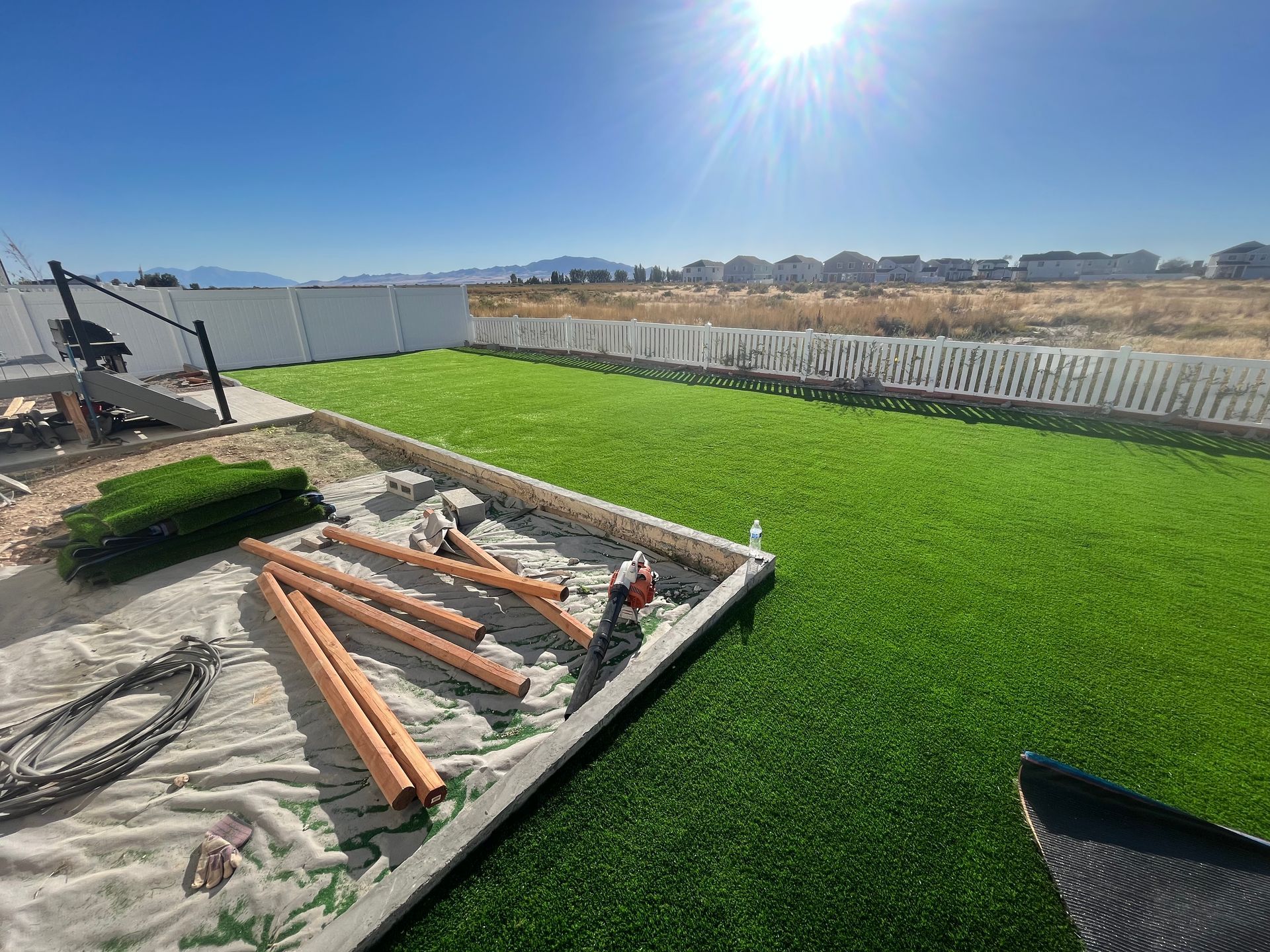 Construction of a backyard play structure on artificial turf with blue sky and a fence.