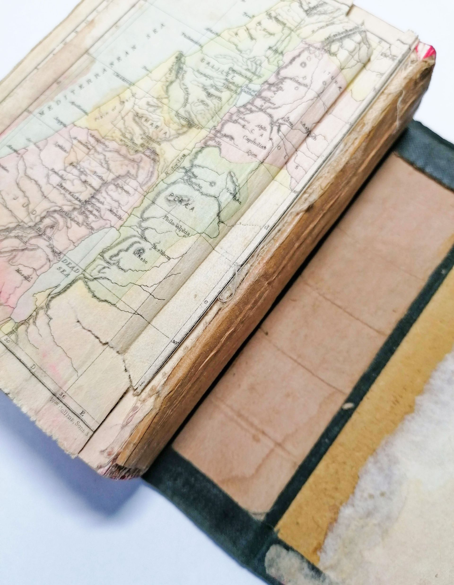 The image shows the back of an old book. A map is the back page of the book and this is ripped and separated from the rest of the book. The spine of the book is very old and the cover of the book has completely separated from the pages of the book. The cover is shown laid flat underneath the pages.