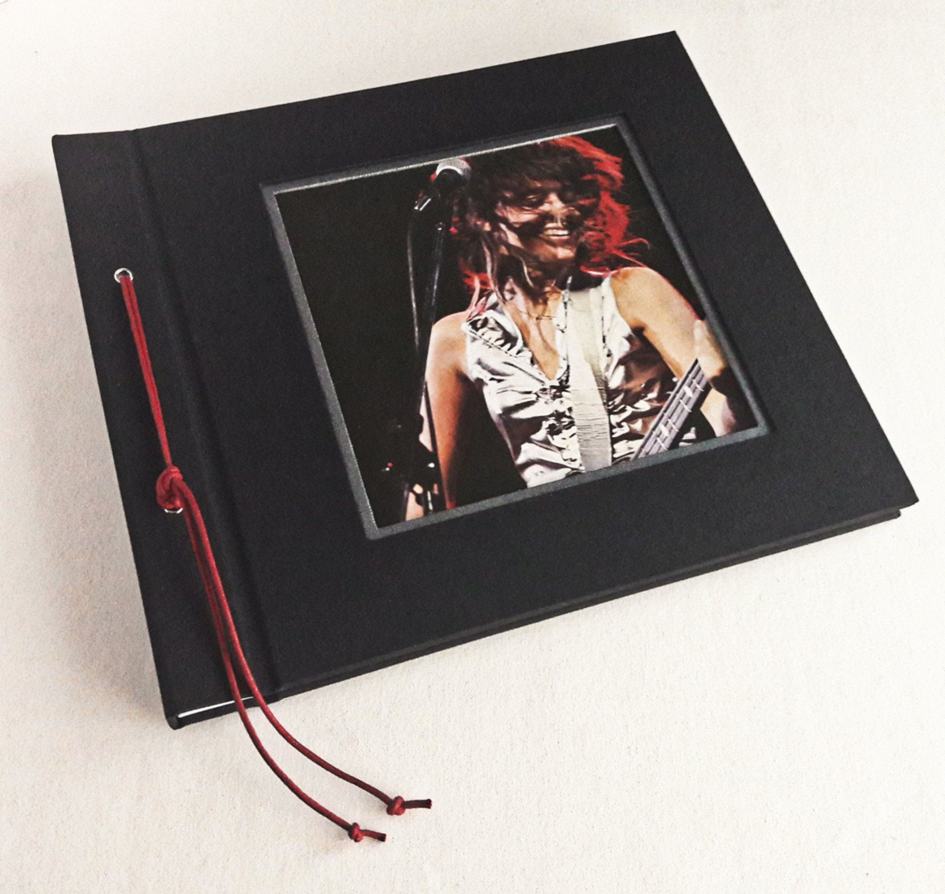 The image shows a bespoke landscape photo album covered in black book cloth with a vintage Suzi Quattro image from a magazine designed within a cut out on the front cover.