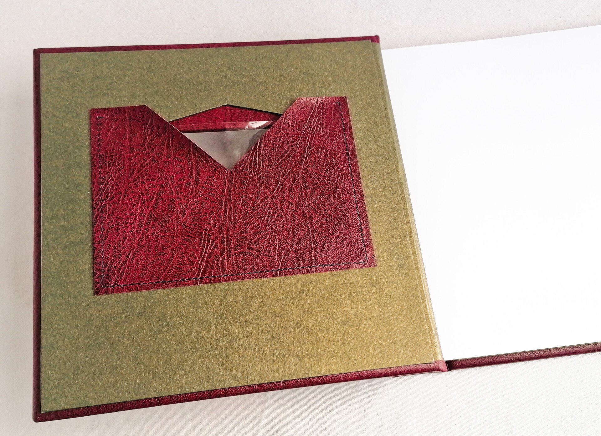 The image shows the front cover of the album opened and the maroon leather album pocket is shown in detail where the photo can be inserted. The album has white pages and the first page can also be seen.