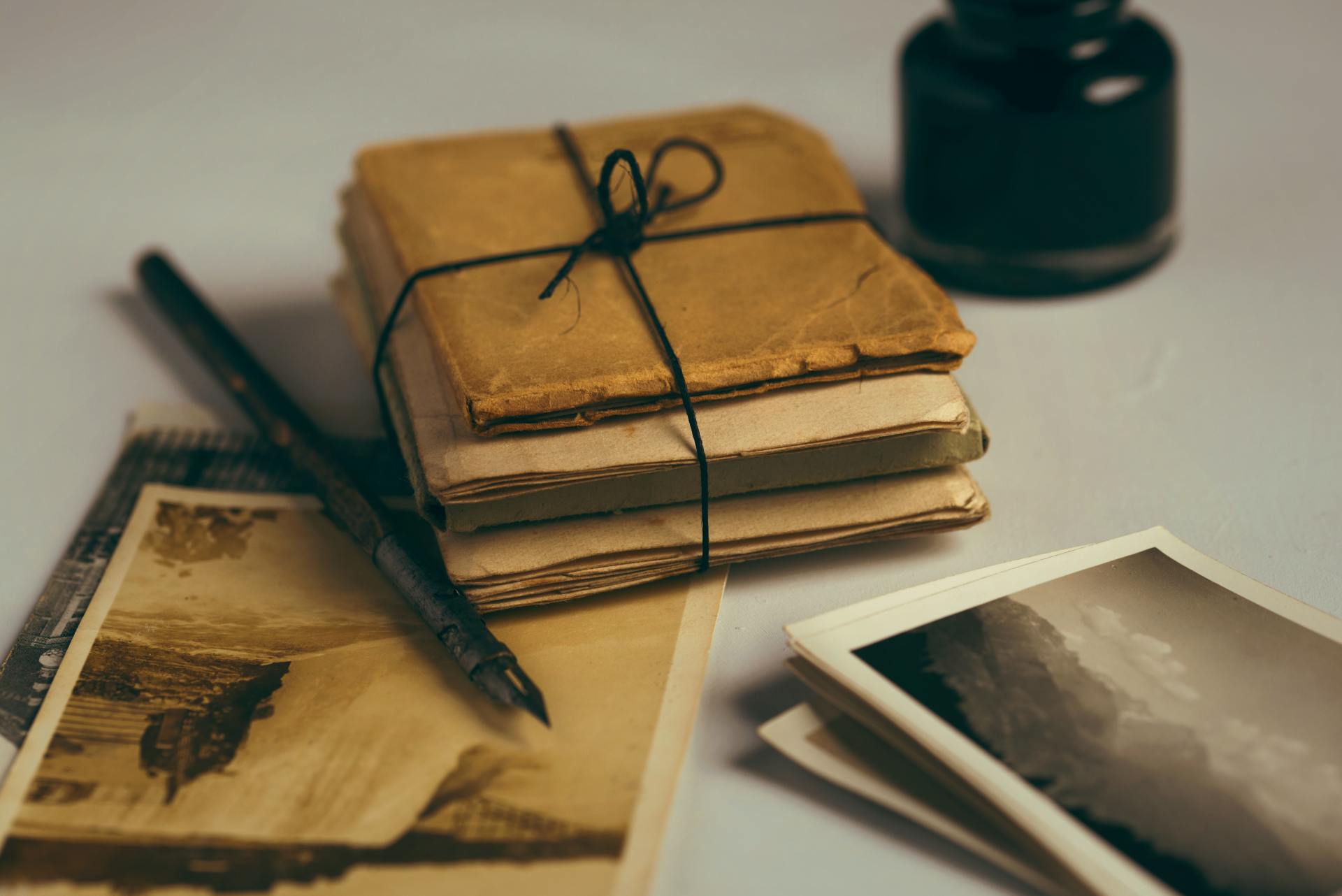 An image of 3 vintage envelopes stacked on top of one another and tied together with thin black string. There is a fountain pen next to them.