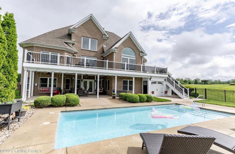 Backyard with pool, multi-story brick house, white trim, balcony, cloudy sky.