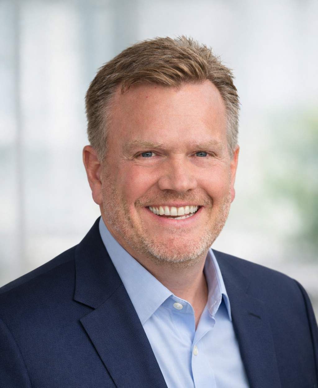 Man in blazer with hands in pockets, smiling.