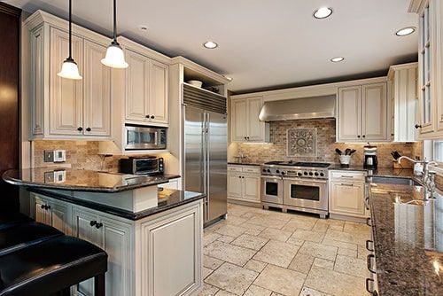 Elegant cream-colored kitchen with stainless steel appliances, marble countertops, and stone-tiled floor.