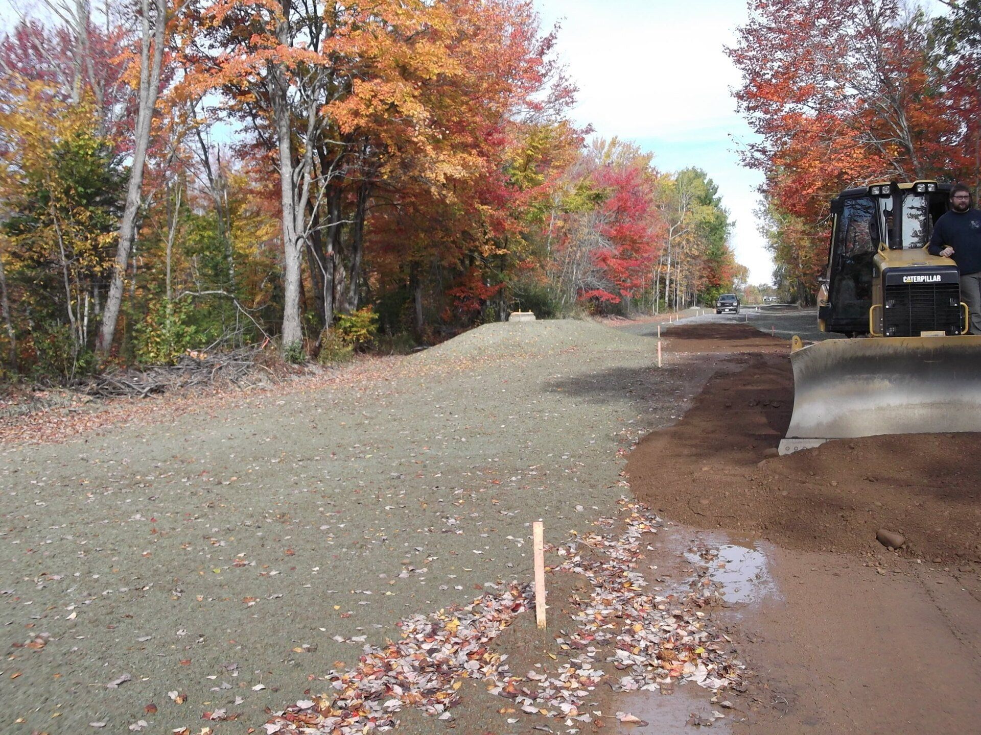 A bulldozer is driving down a dirt road with trees in the background