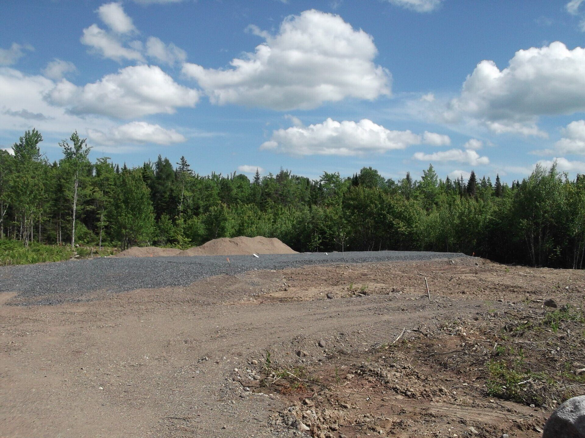 A dirt road with trees in the background and a blue sky with clouds
