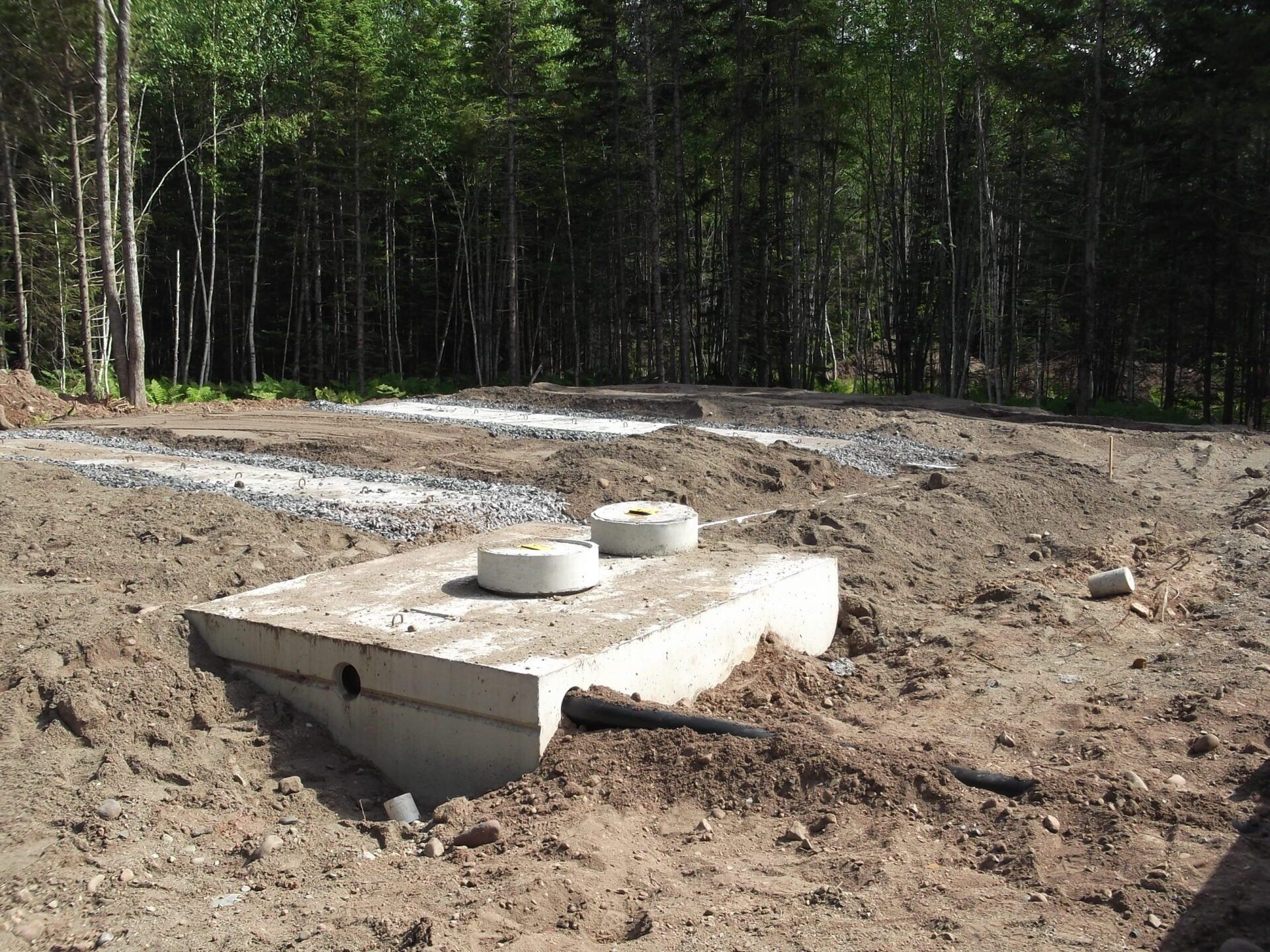 A septic tank is sitting in the middle of a dirt field surrounded by trees.