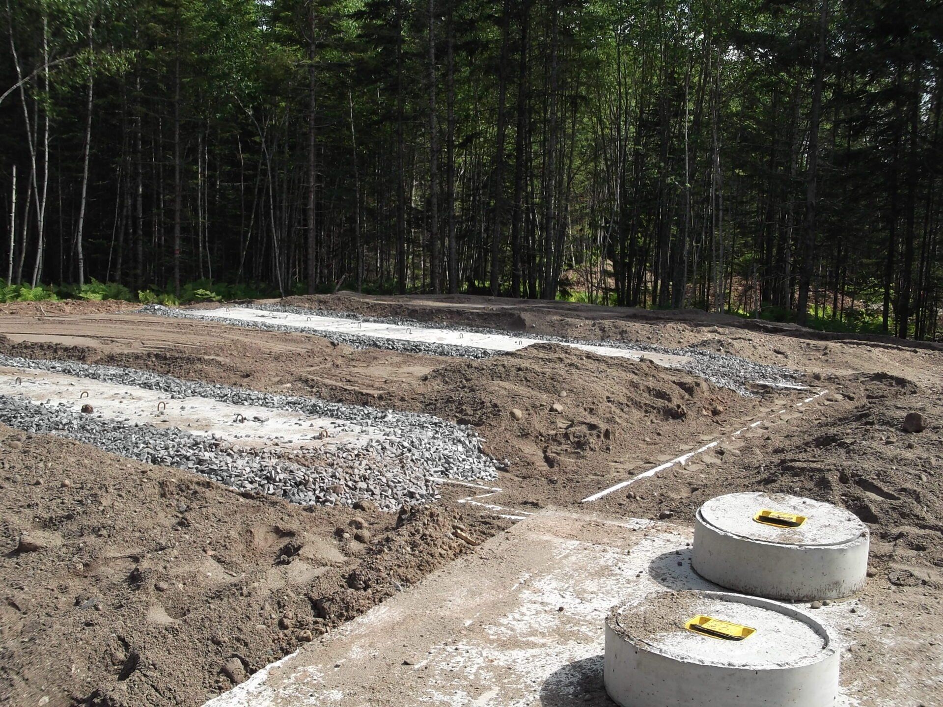 Two septic tanks in a dirt field with trees in the background