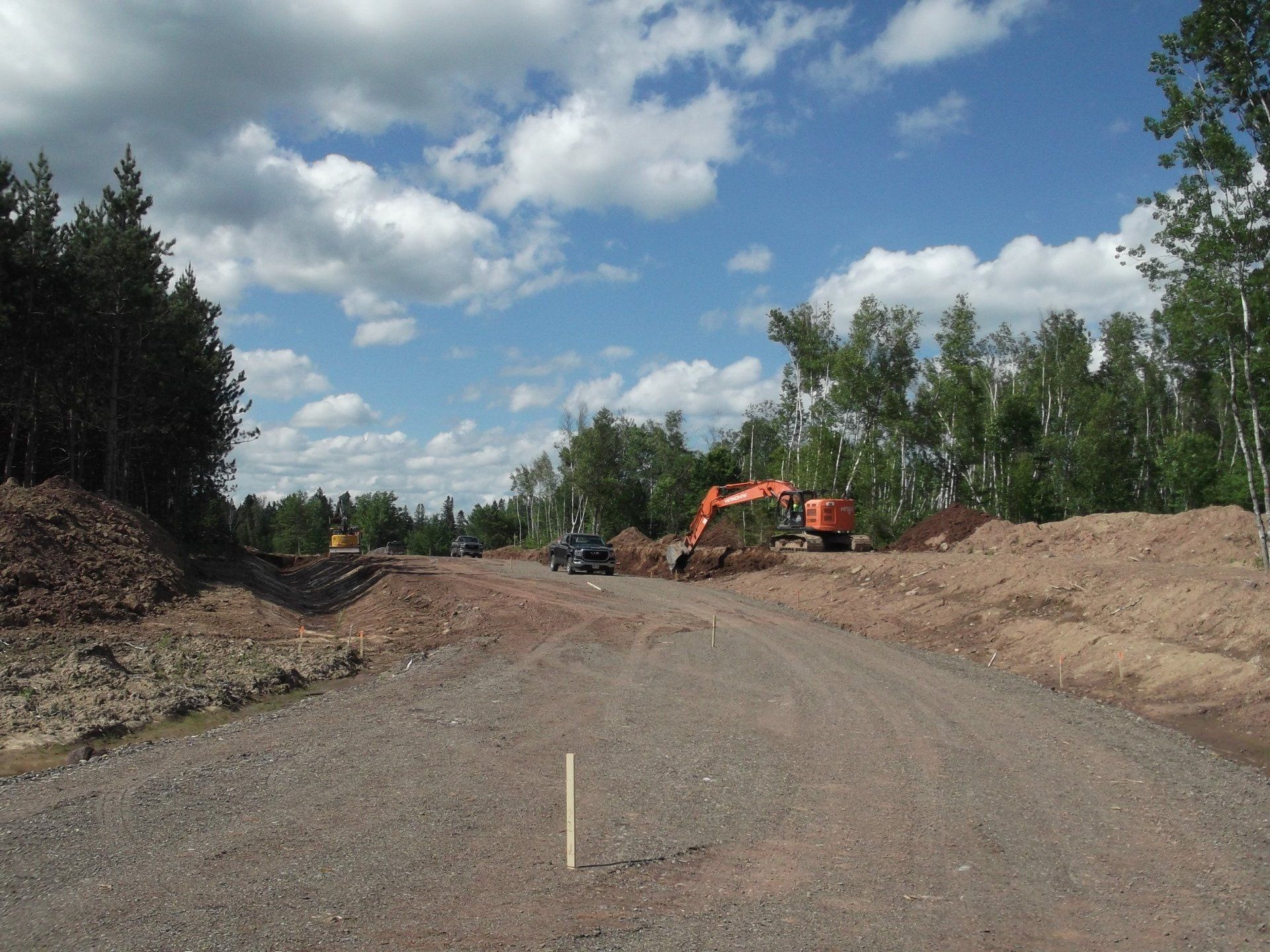 An excavator is driving down a dirt road with trees in the background