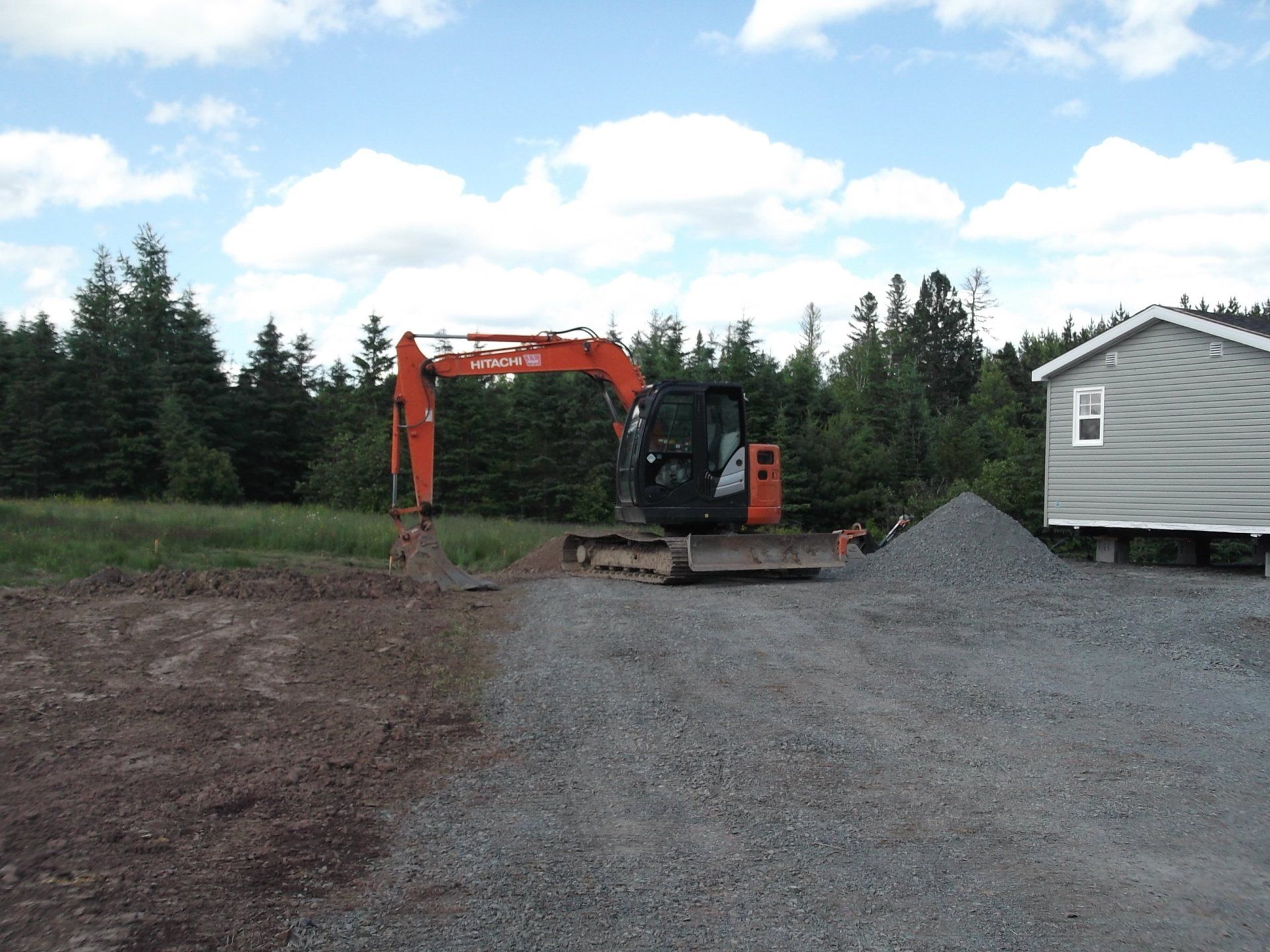 An orange excavator is in a gravel area next to a house