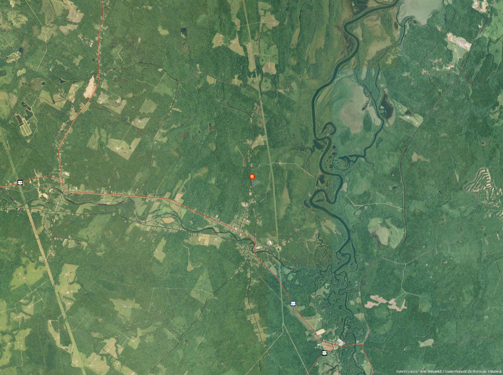 Overhead view of a dense green forest with a winding river, a few clearings, and a road.