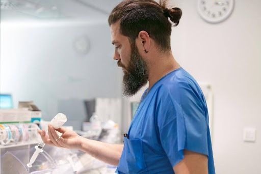 Medical worker in blue scrubs holding vial and syringe in a clinical setting.