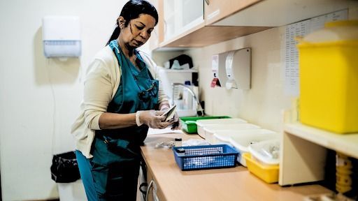 Person in blue scrubs, examining a vial and syringe in a medical setting.