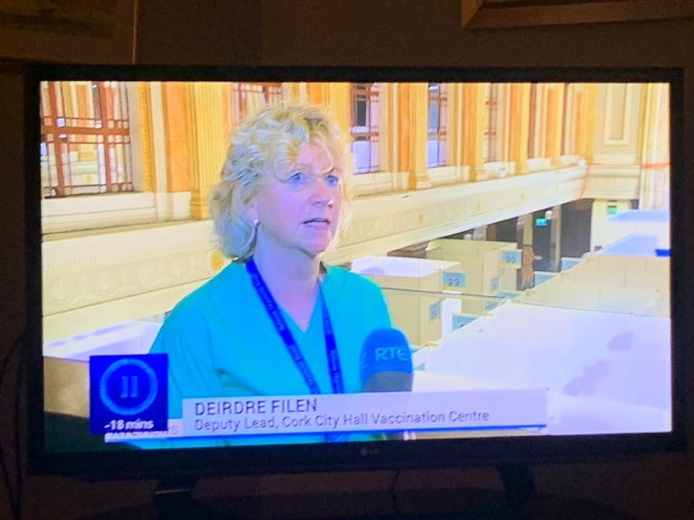 A woman, Deirdre Filen, in scrubs, speaks in a news interview at Cork City Hall Vaccination Centre.