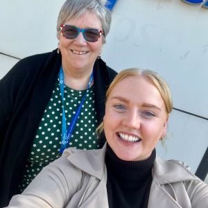 Two smiling women posing for a selfie. One wearing a green polka dot shirt and sunglasses, the other in a tan coat.