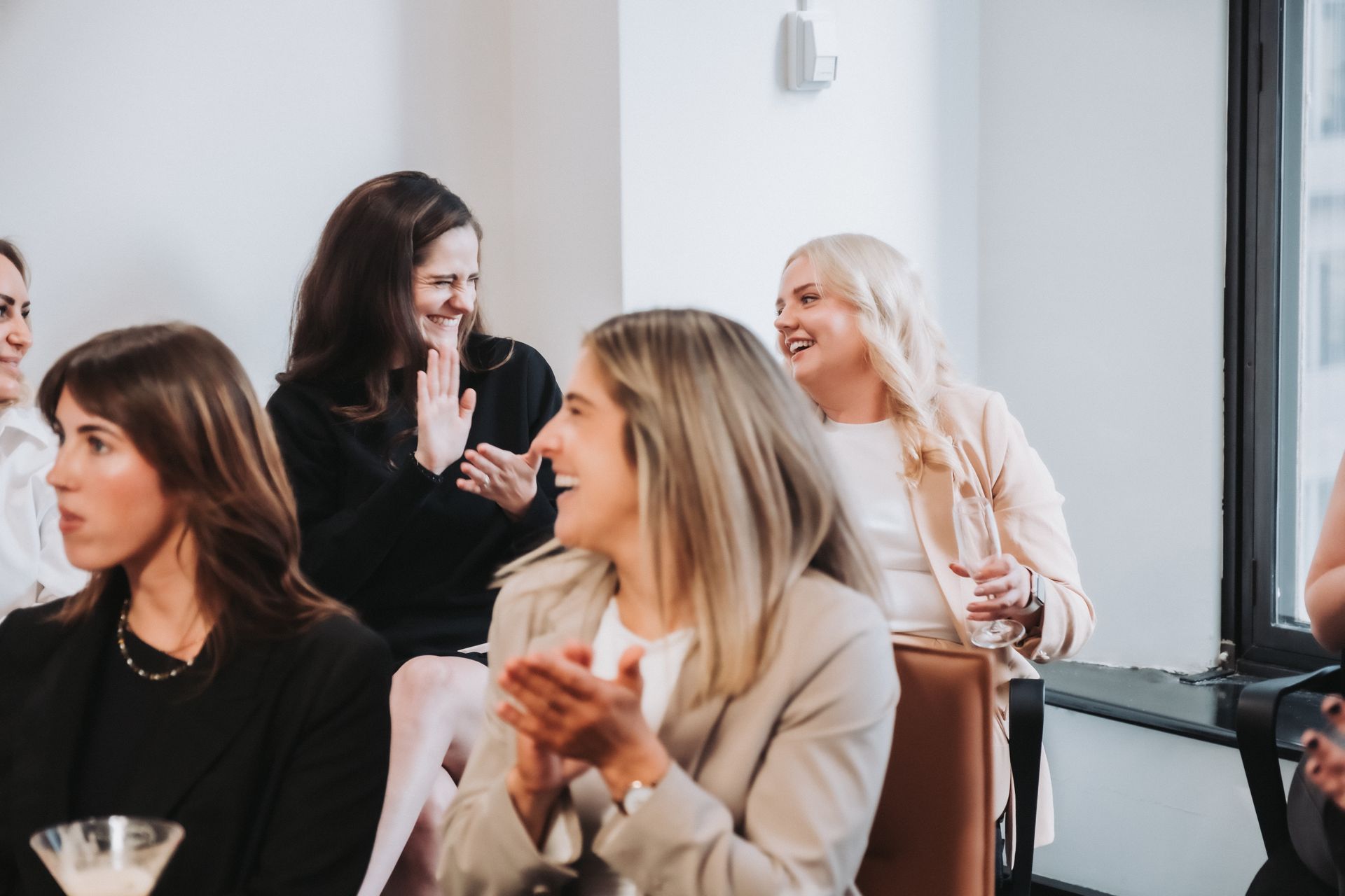 Women in business attire laughing and applauding in a bright room.