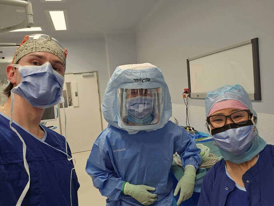 Two people in hospital PPE and face shields pose indoors with a text sign between them.