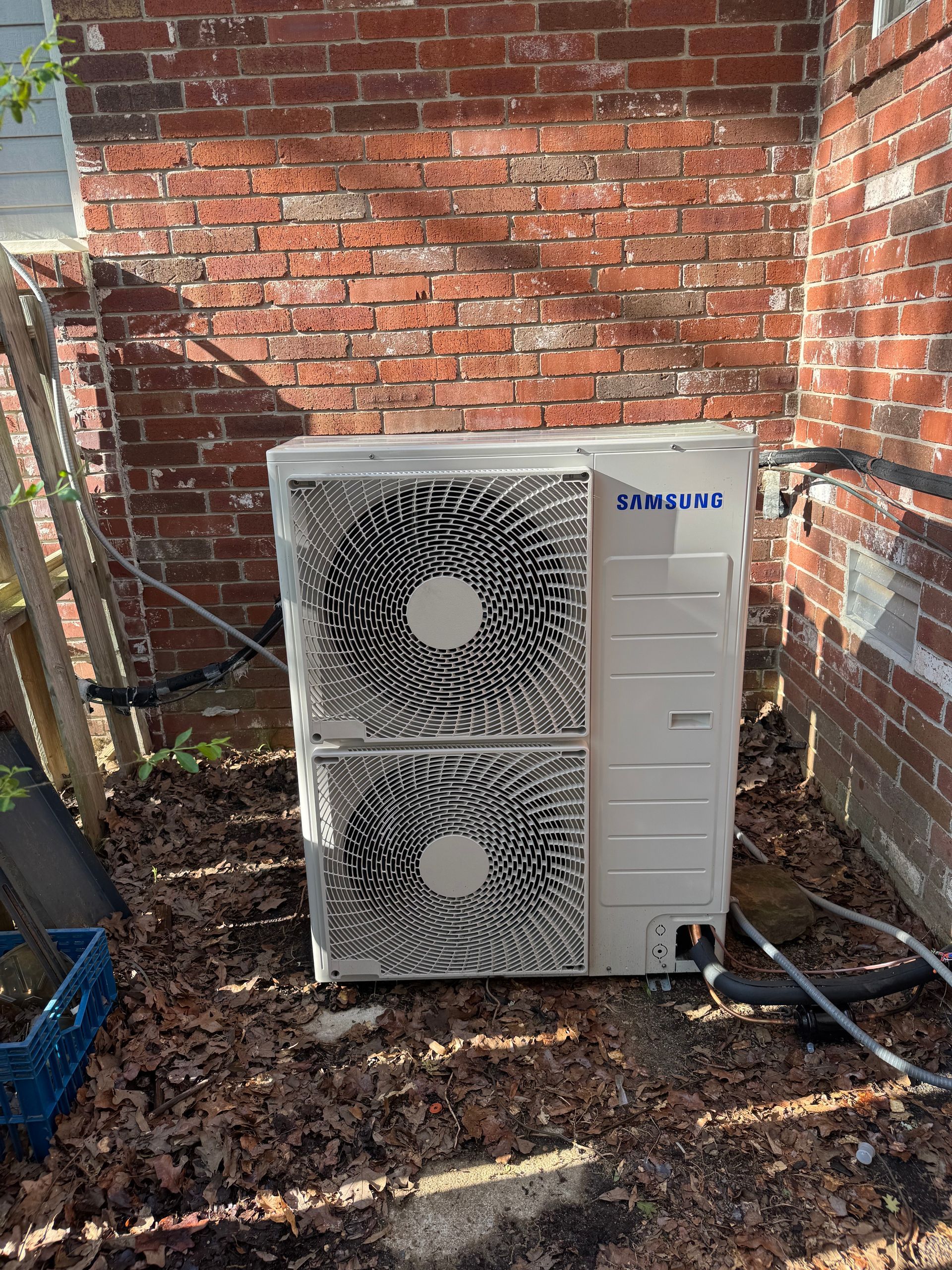 A samsung air conditioner is sitting outside of a brick building.