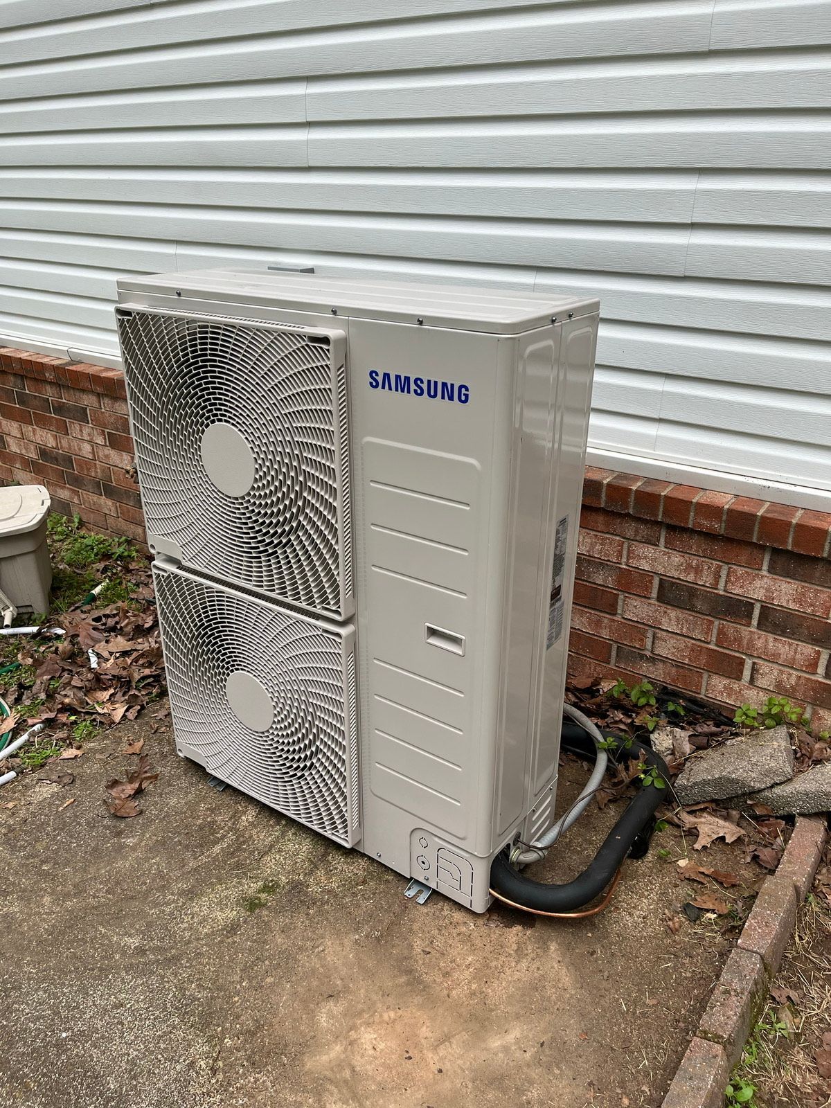 A samsung air conditioner is sitting outside of a house.