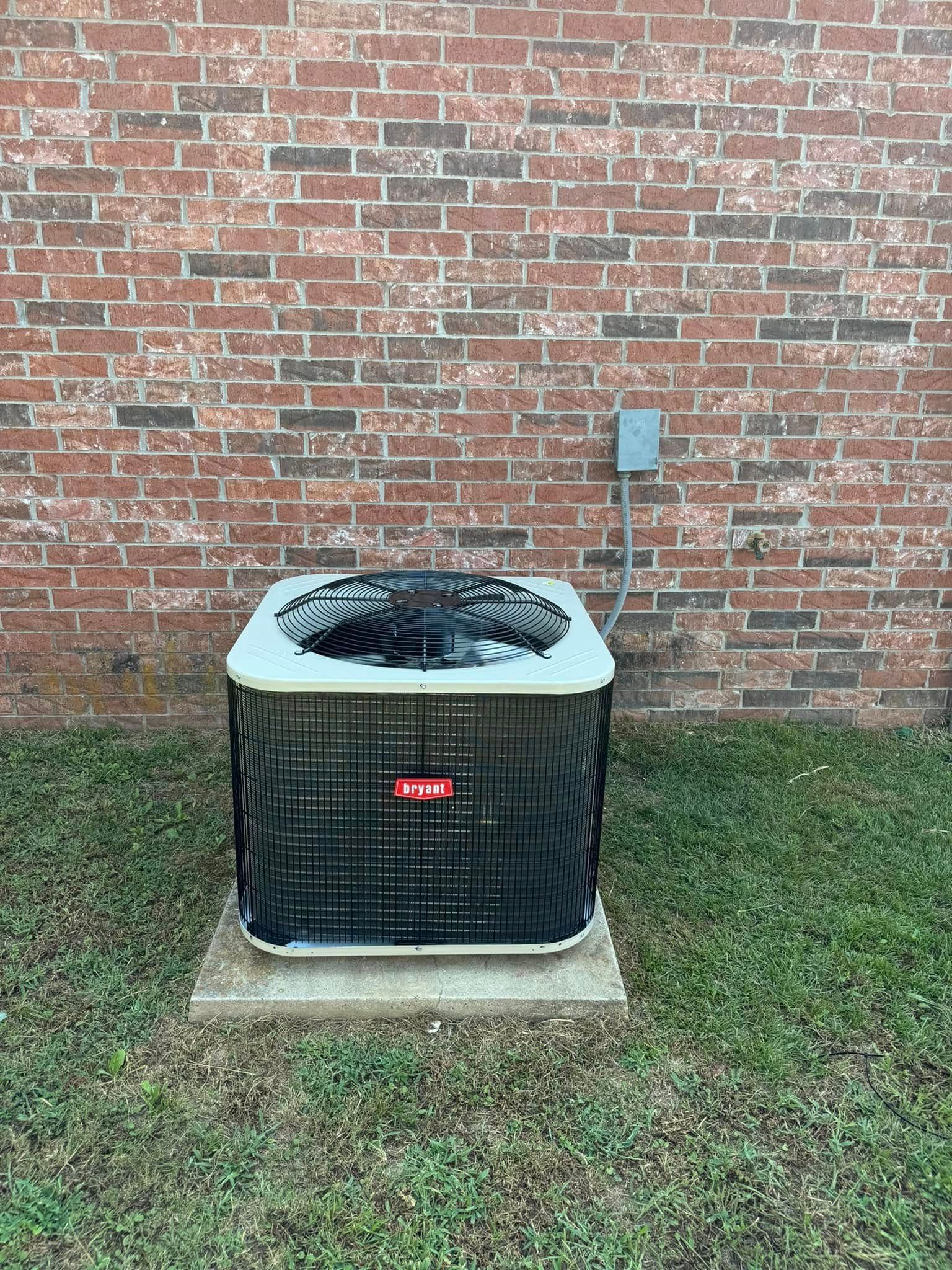 An air conditioner is sitting in the grass in front of a brick wall.