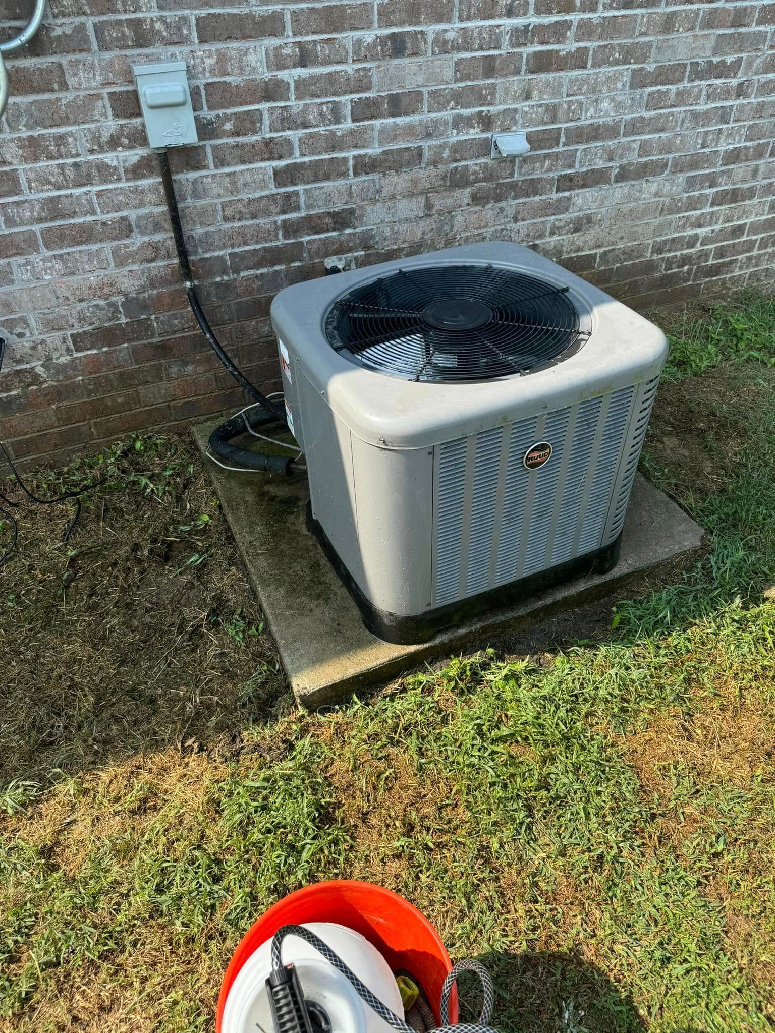 An air conditioner is sitting on top of a concrete platform next to a brick wall.