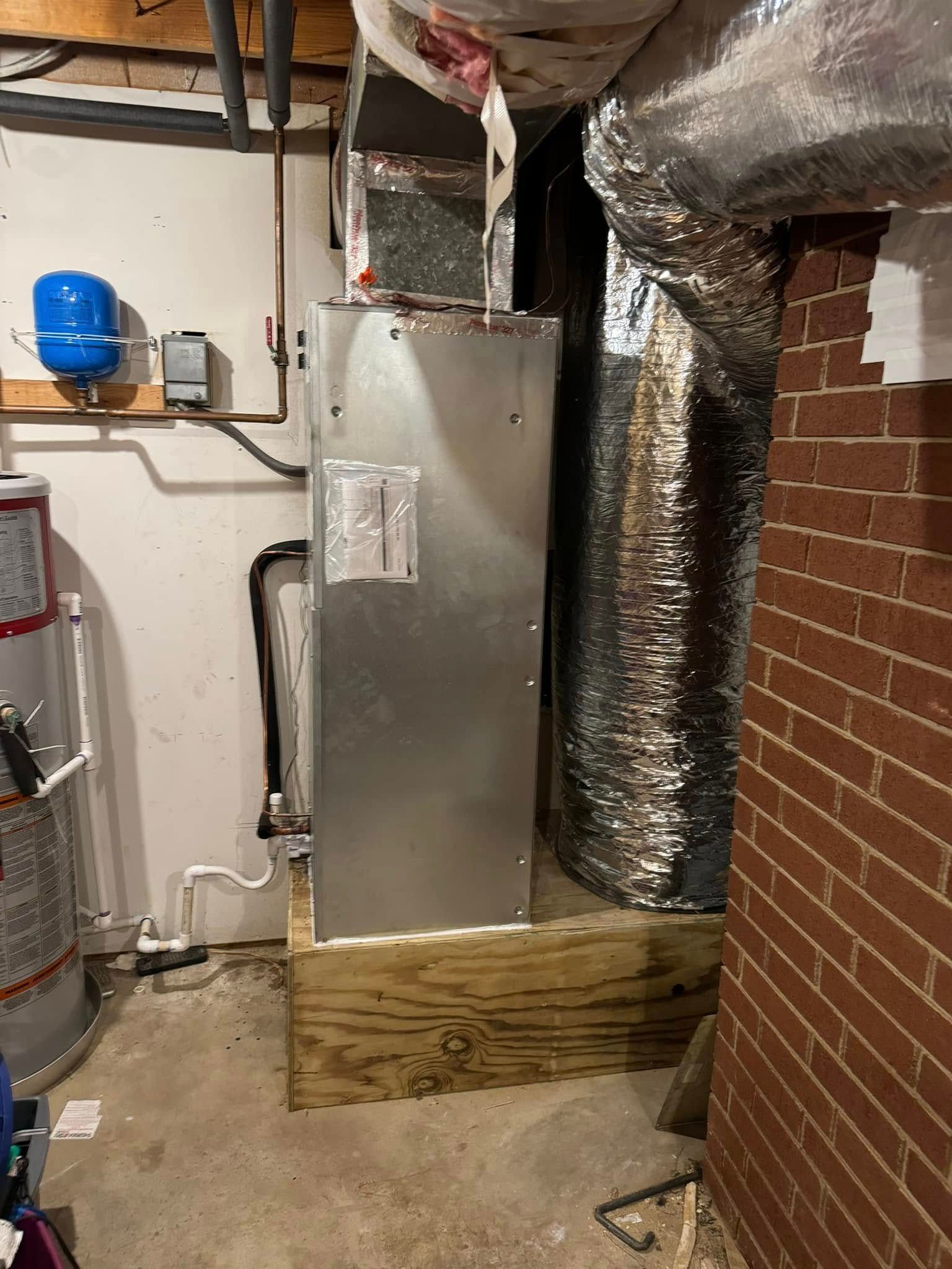 A boiler is sitting in a basement next to a brick wall.