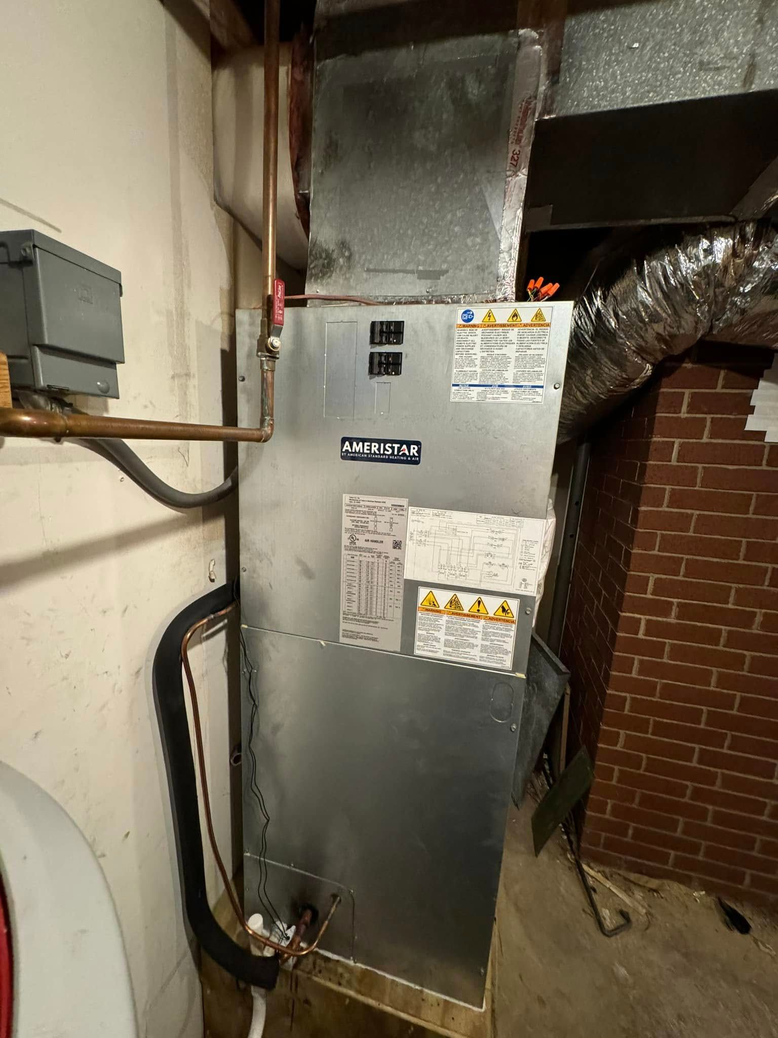 An air conditioner is sitting in a basement next to a brick wall.