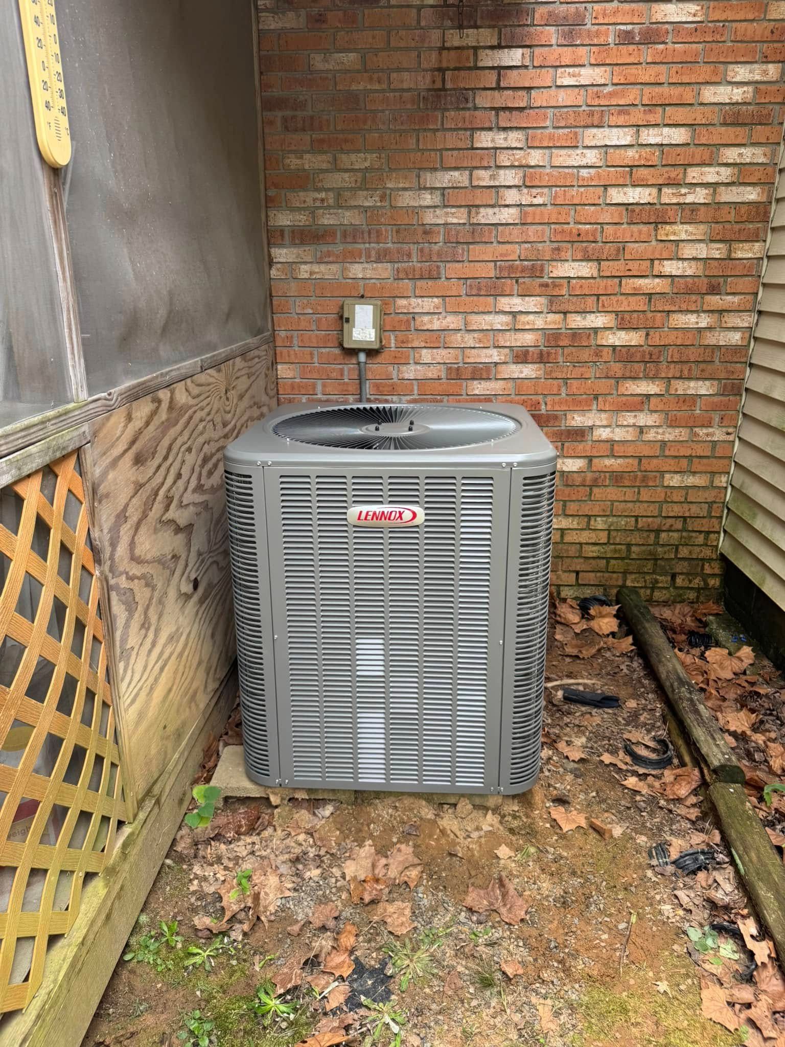 An air conditioner is sitting in a corner of a brick building.