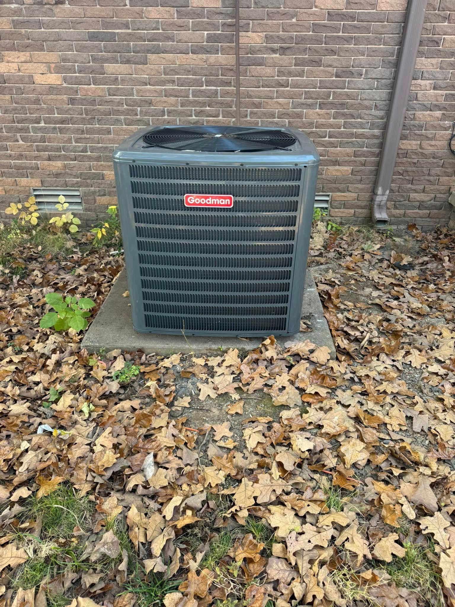 An air conditioner is sitting on top of a pile of leaves in front of a brick building.