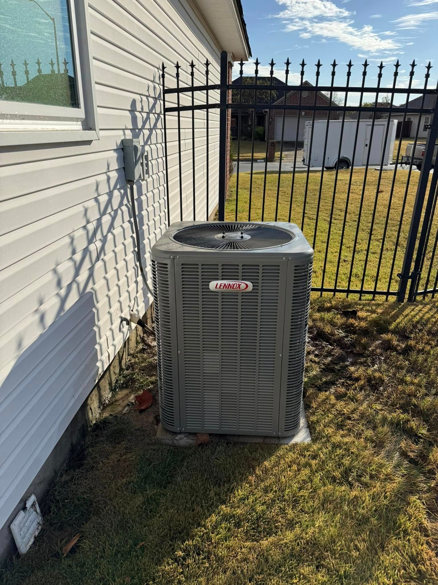 An air conditioner is sitting on the side of a house next to a fence.