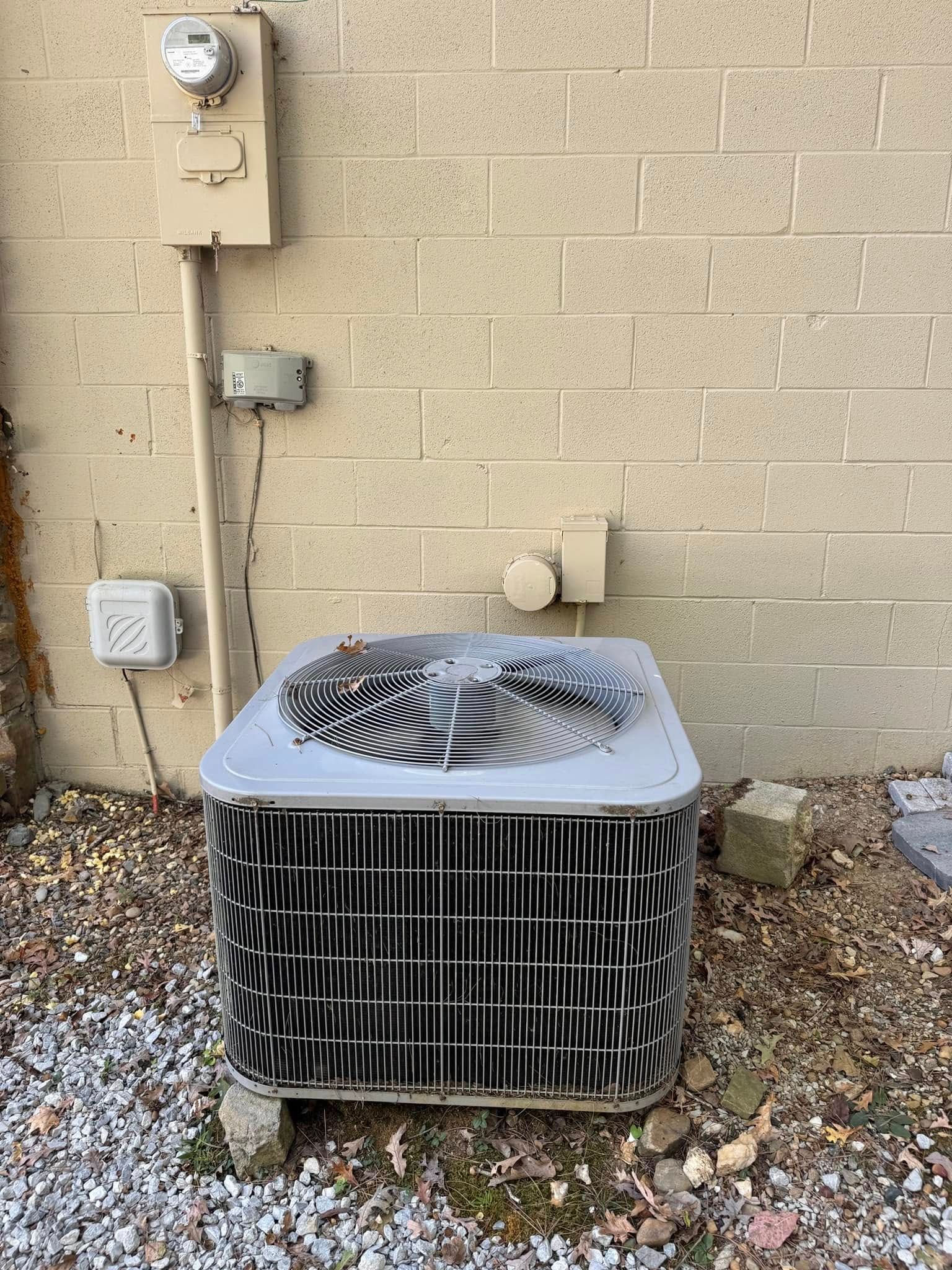 An air conditioner is sitting in front of a brick wall.