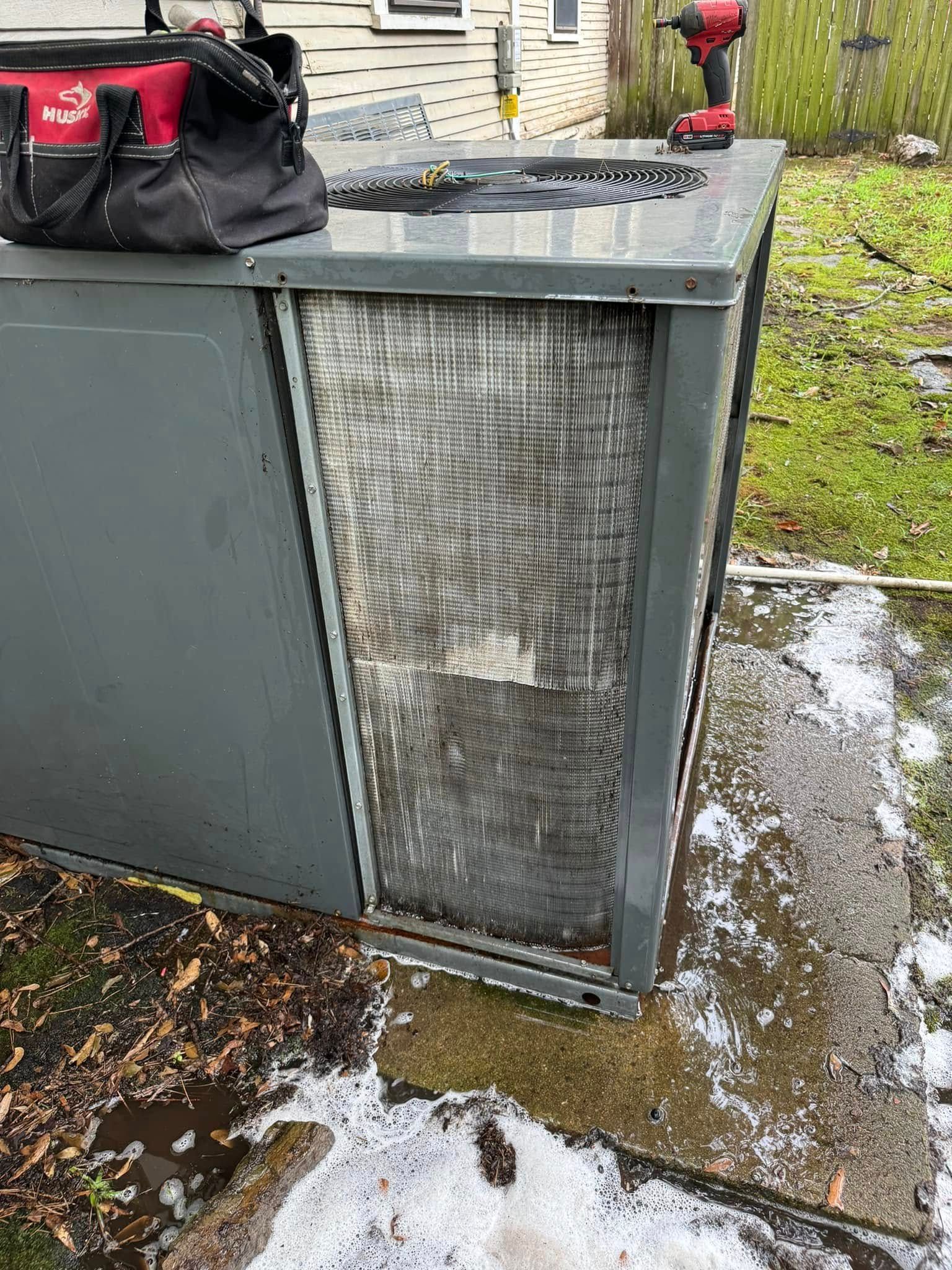 An air conditioner is sitting on the ground next to a drill and a tool bag.