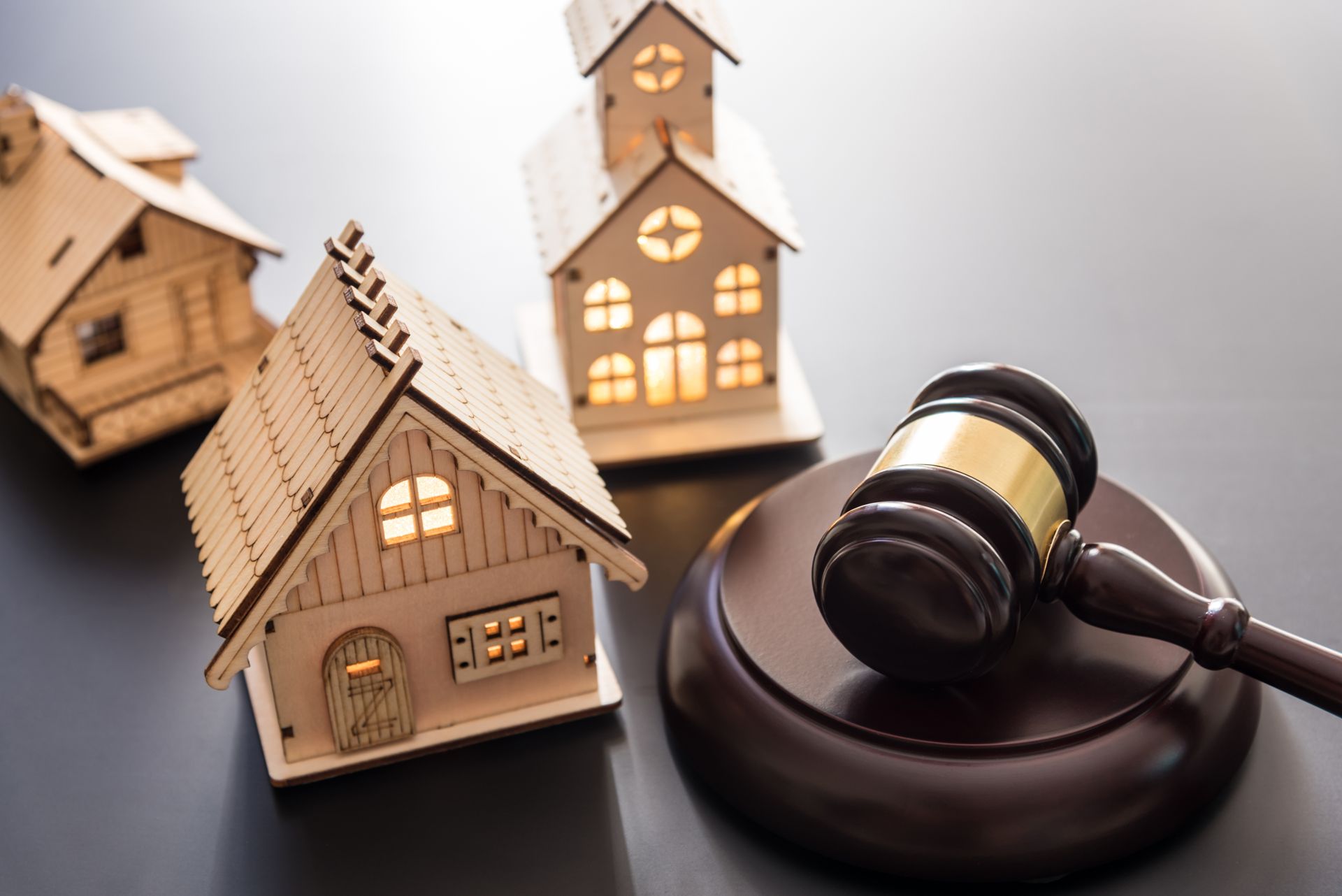 Miniature houses near a gavel on a dark surface, symbolizing a real estate auction.