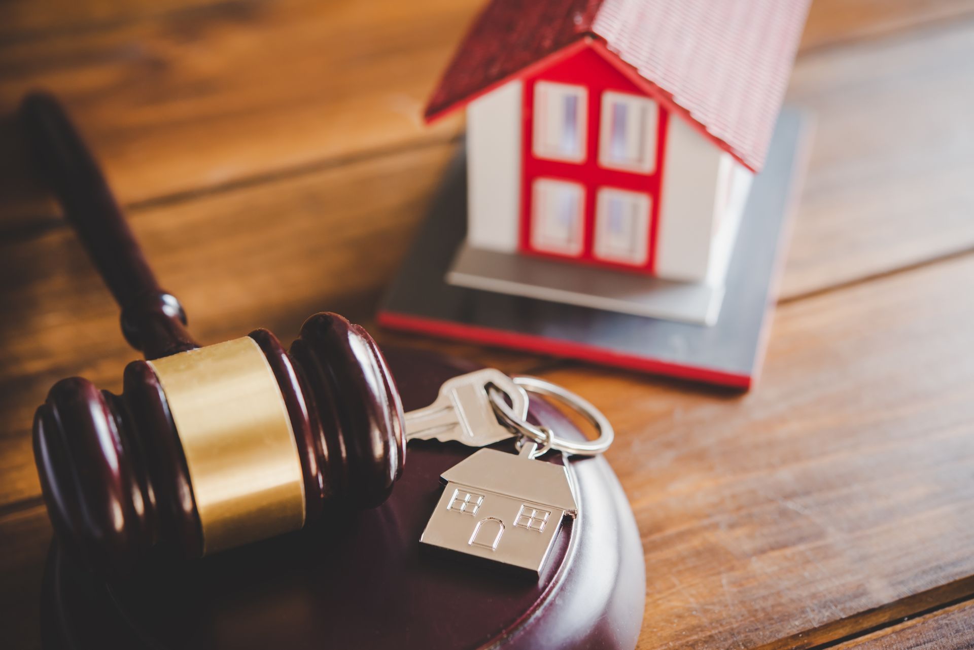 A judge 's gavel , keys and a model house on a wooden table.