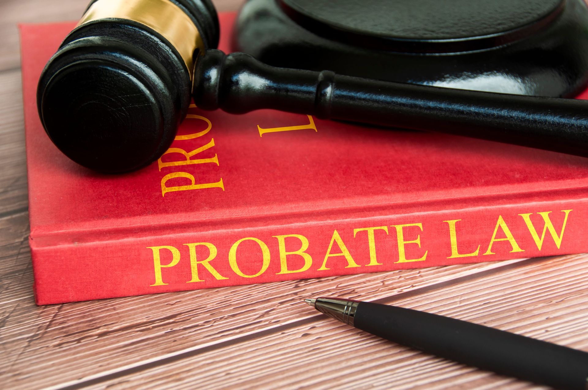 Black gavel on red probate law book beside a pen on a wooden desk