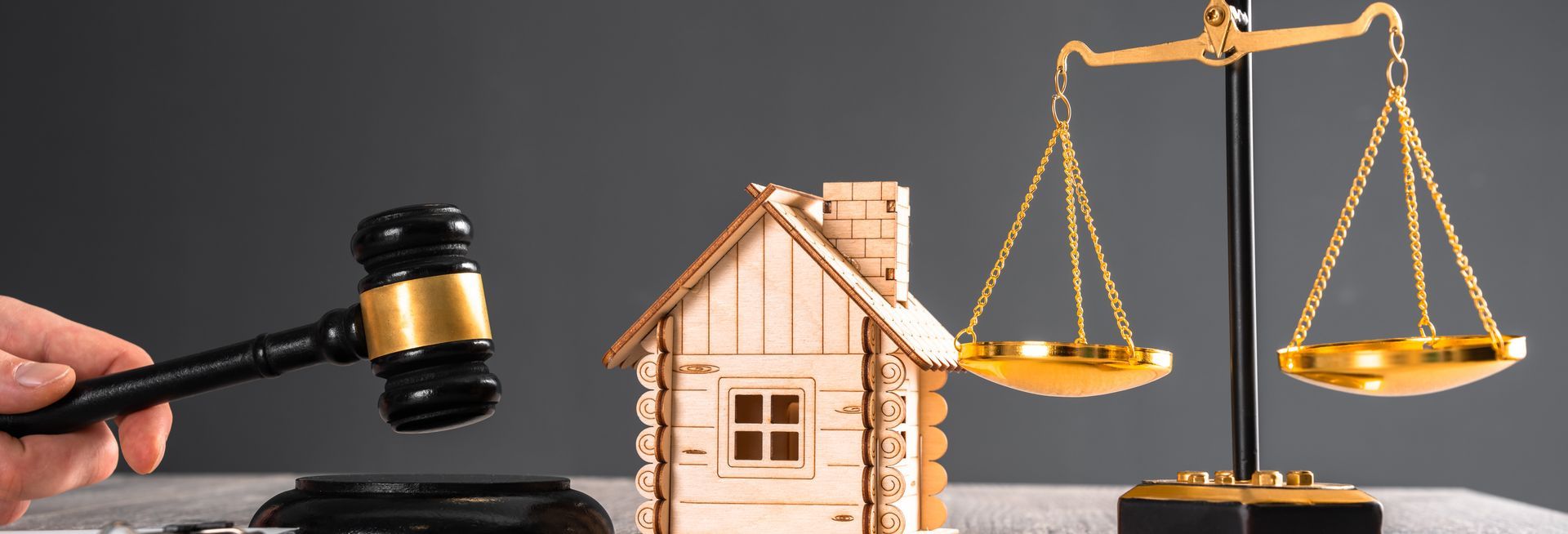 A gavel, house model, and scales of justice, symbolizing real estate law against a gray backdrop.