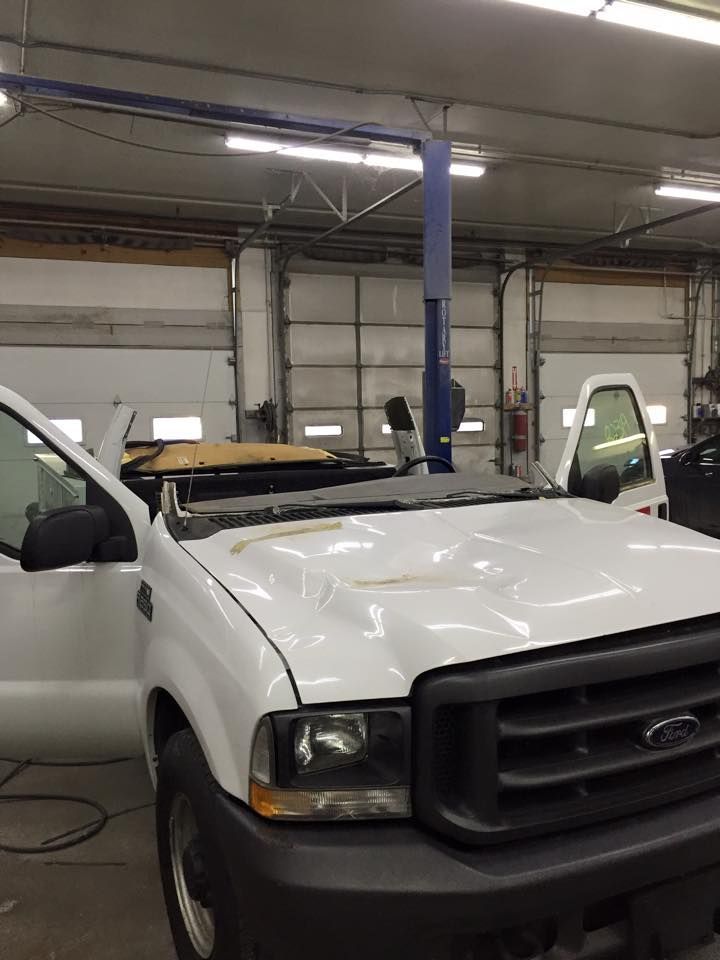 A white truck with a damaged hood is parked in a garage.