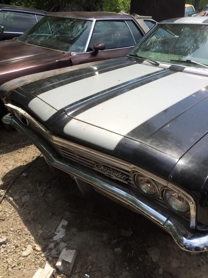 A black car with white stripes on the hood is parked next to another car.