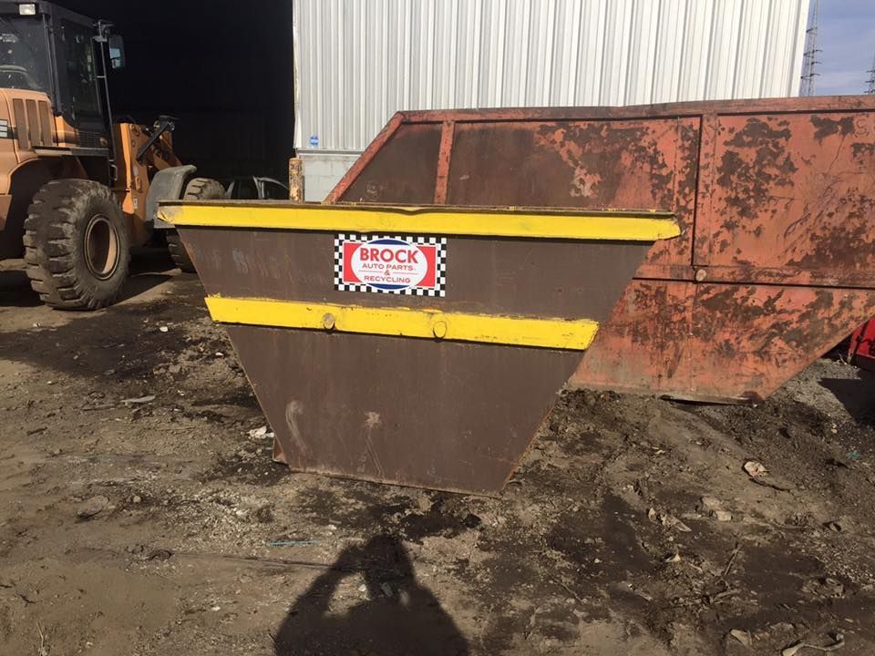 A dumpster is sitting in the dirt in front of a building.