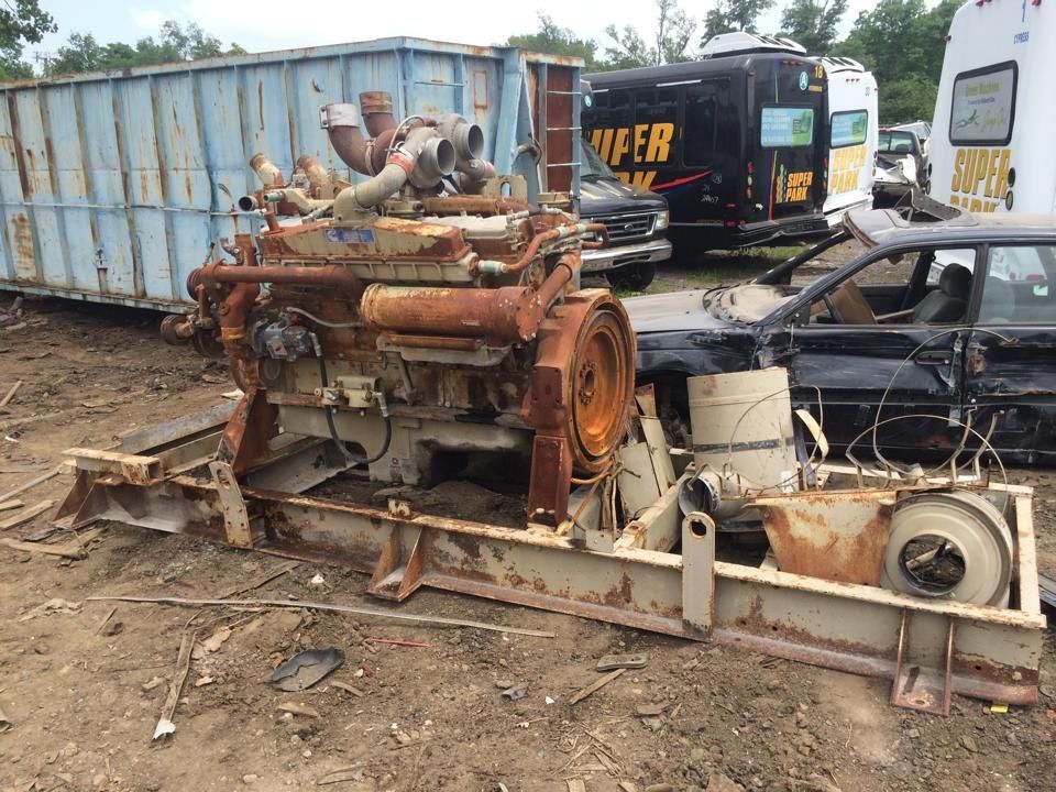 A rusty engine is sitting in a junkyard next to a car.