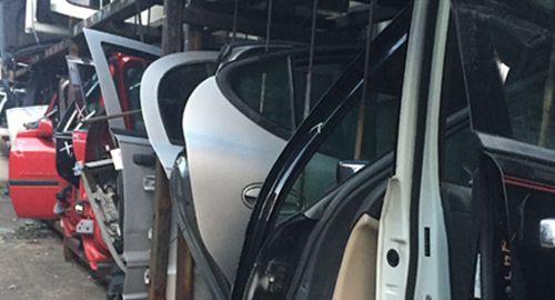 A bunch of car doors are stacked on top of each other in a garage.