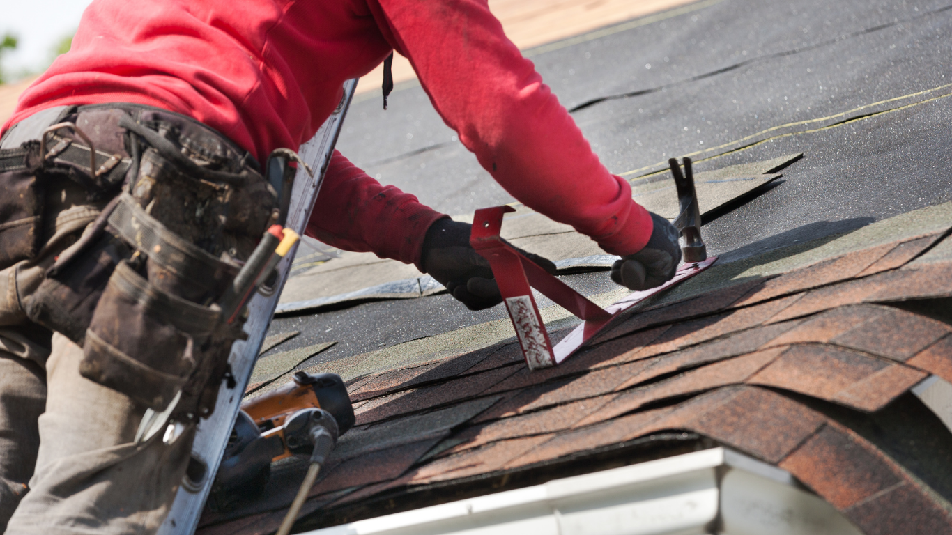 A man is standing on a ladder working on a roof.