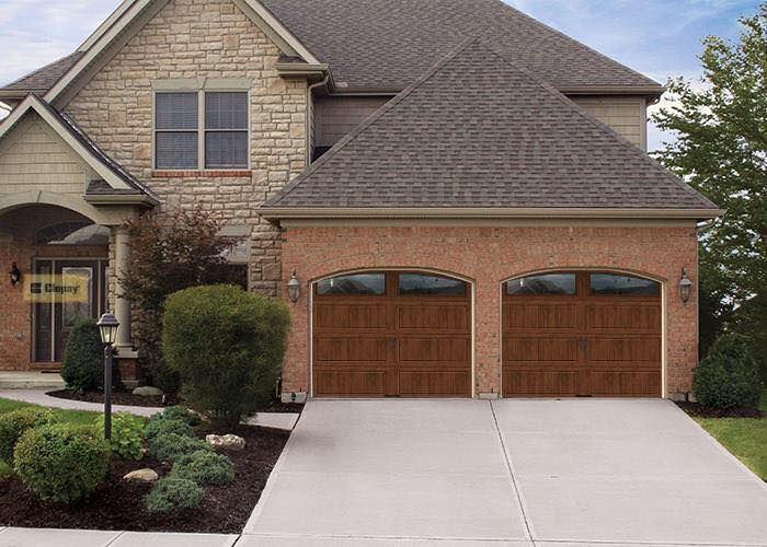 Two-story house with brick and stone facade, two-car garage with brown doors, and concrete driveway.