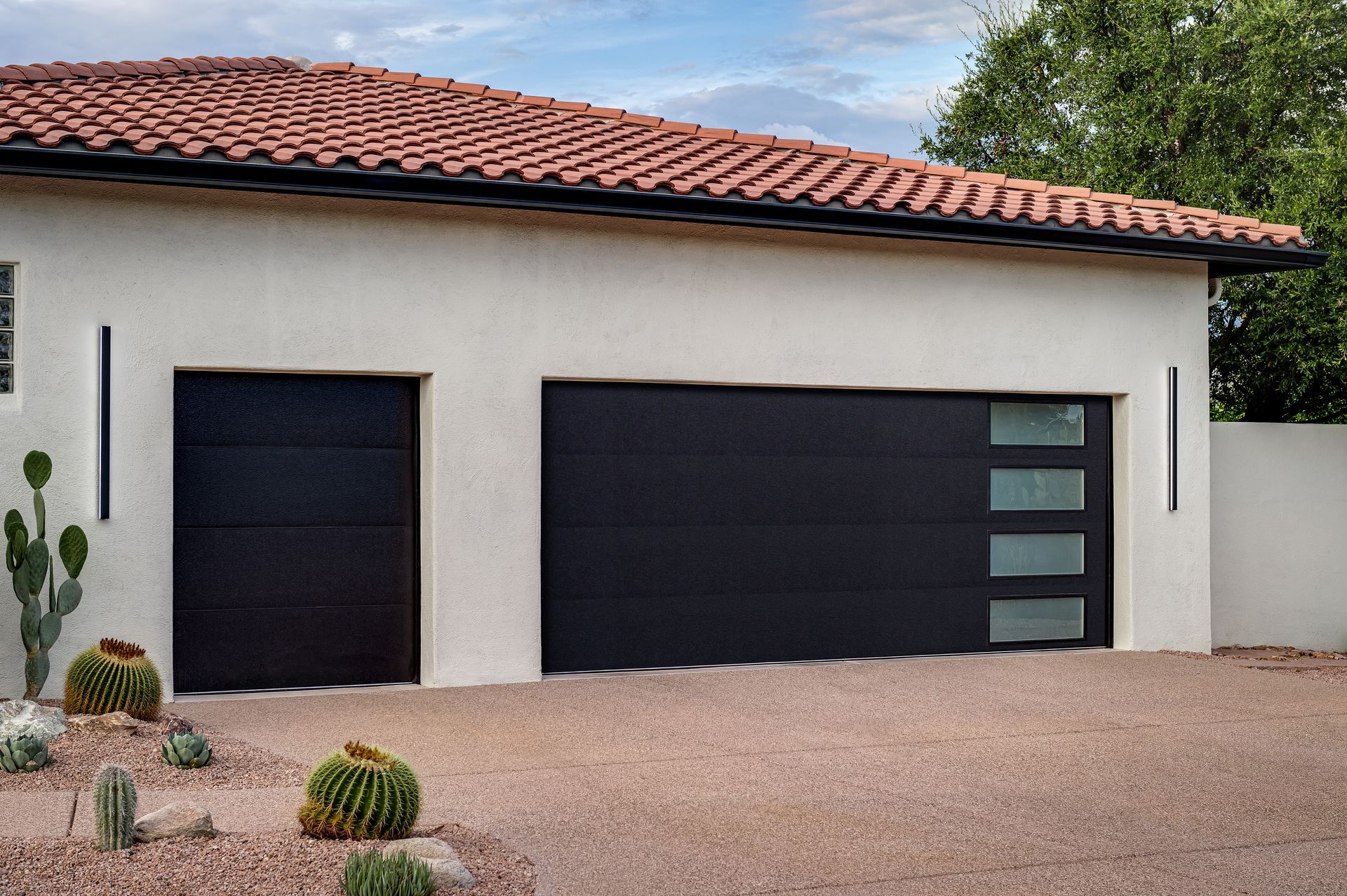 Black garage doors on a stucco house with a tiled roof.  Desert landscaping.