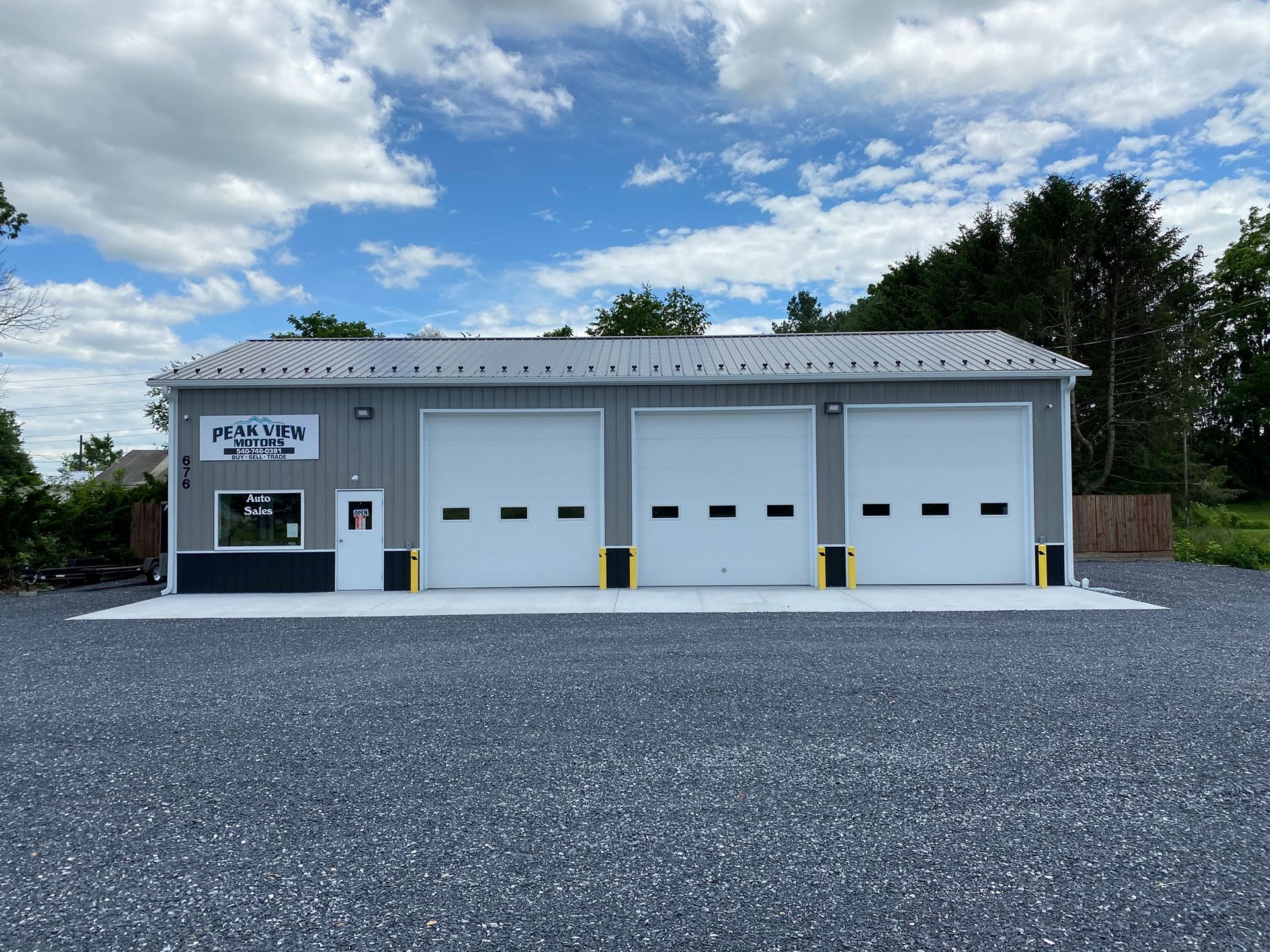 Exterior of a gray auto repair shop with three garage doors. Sky with clouds above.