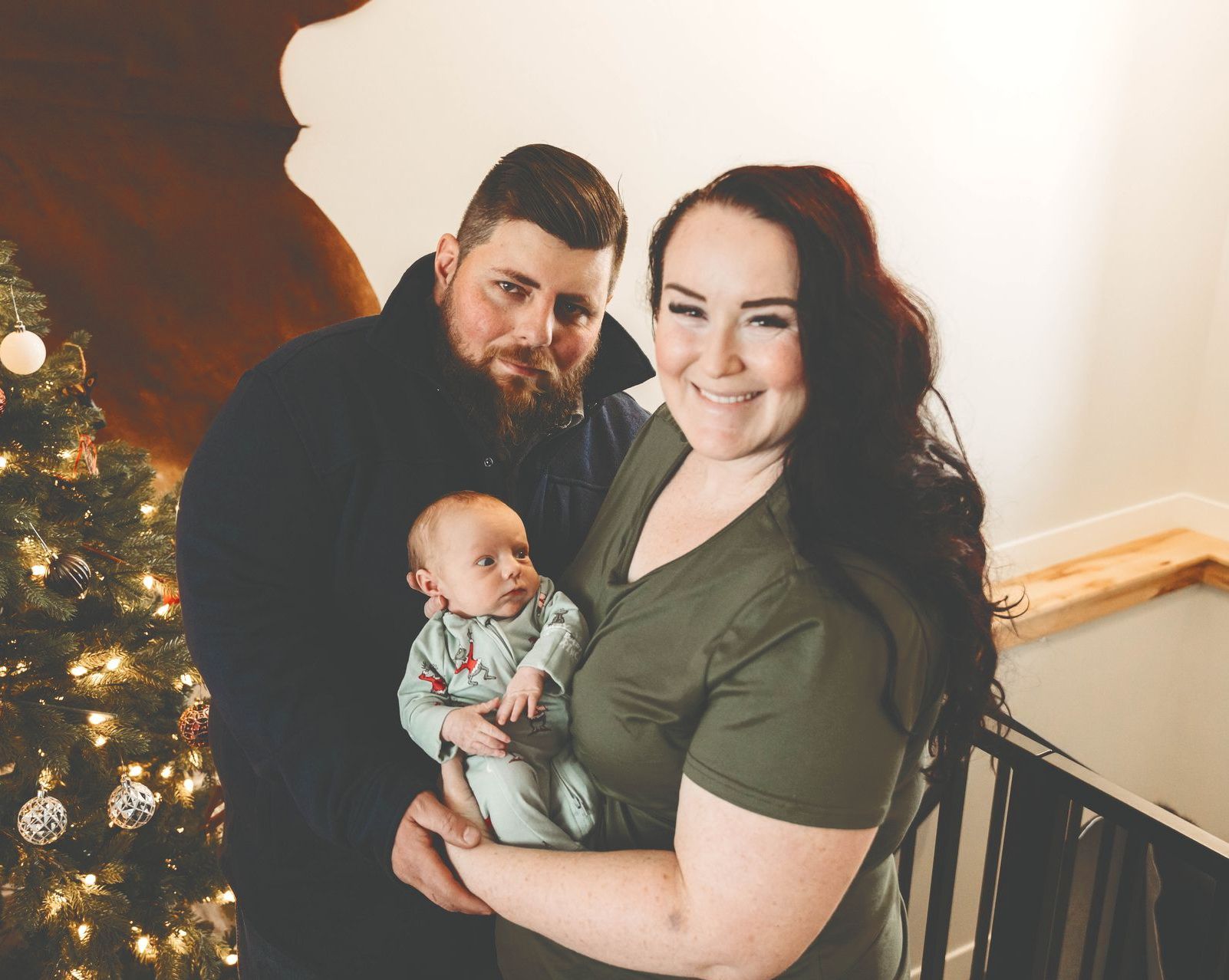 A man and woman are holding a baby in front of a christmas tree.